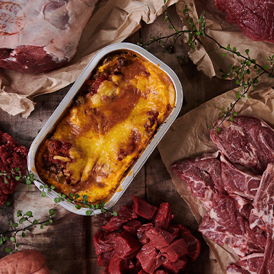 Arial view of various meat cuts, a prepared lasagne and herb garnishes.