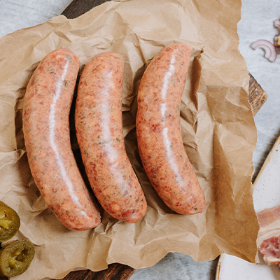3 sausages sit on brown paper with Jalapeno peppers on the left and smoked beef brisket on the right.