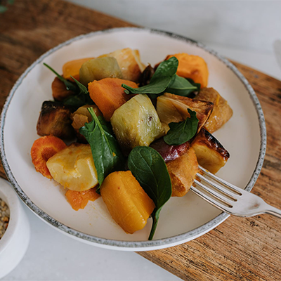 Waipawa Butchery Kitchen plate of roasted colourful vegetables in a white bowl, with a fork, sitting on a cutting board.