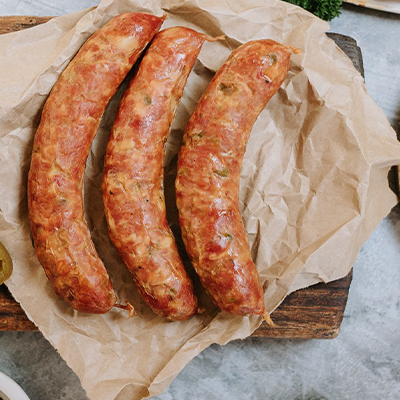 3 cheese kransky sausages lay on some brown paper. To their left, we see some sliced jalepeno peppers and to the right some cubed cheese on a board.